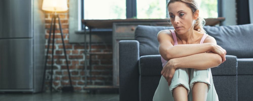 Unieważnianie emocji Jakie są źródła unieważniania emocji w związku - smutna kobieta siedzie na podłodze rozmyślając, dlaczego partner znowu unieważnił jej emocje - Marita Woźny