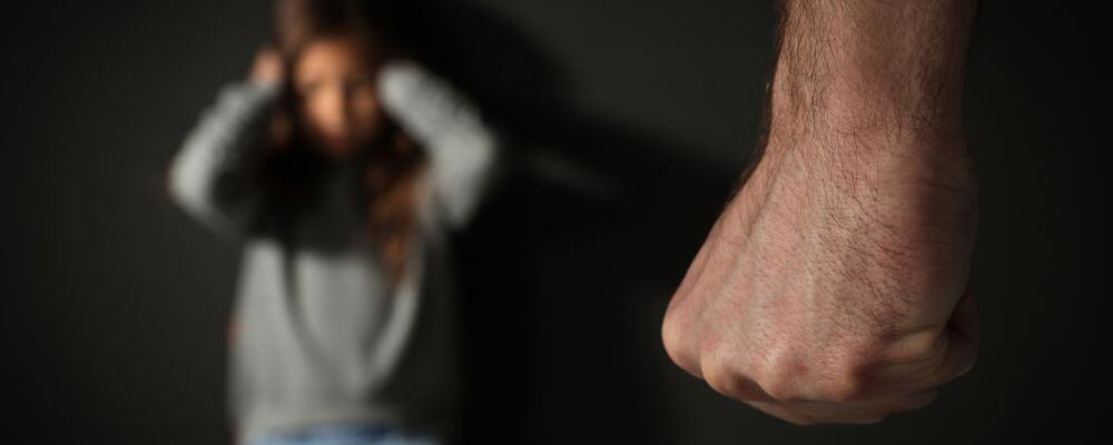 Przemoc domowa i przemoc psychiczna wobec dzieci – jak ją rozpoznać i przerwać? - dziecko w tle siedzi przestraszone, przed nim zaciśnięta pięść opiekuna - blog Marita Woźny
